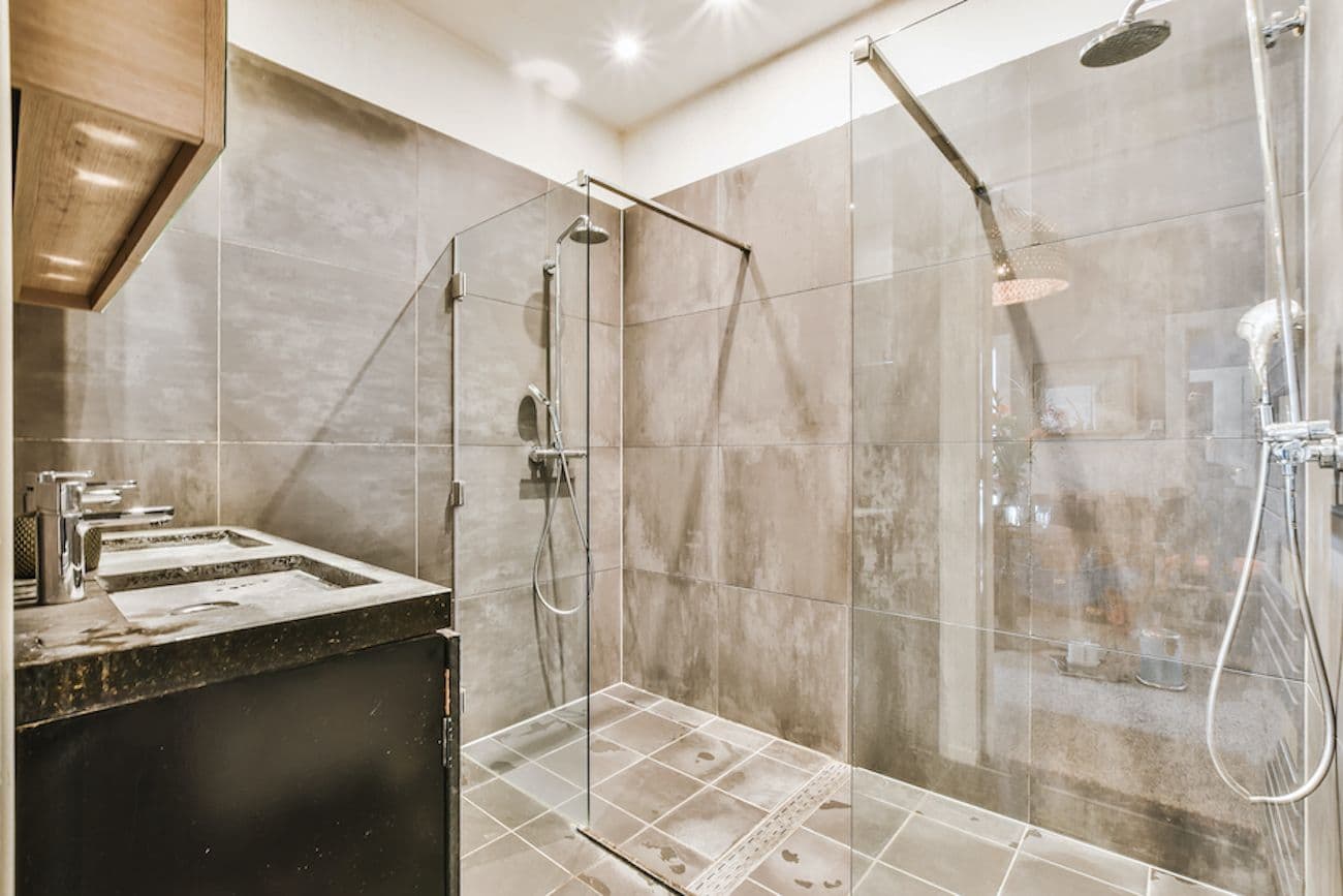 Modern bathroom with frameless glass shower enclosure, dual showerheads, dark vanity with marble countertop, and recessed lighting