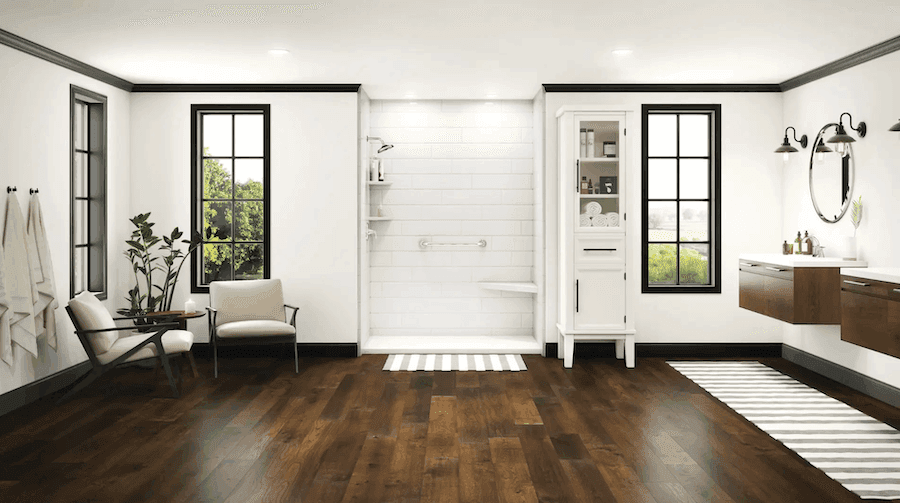 Modern bathroom showroom with dark wood flooring, white walls, black-trimmed windows and doors, walk-in shower, floating vanity with wood cabinets, and seating area with potted plant
