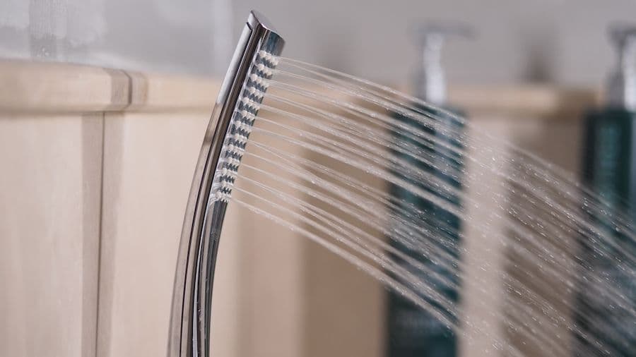 Shower head spraying water with streams of water visible against a blurred bathroom background