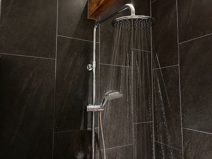 Modern shower system with rain showerhead and handheld spray mounted on dark tiled wall, both actively dispensing water