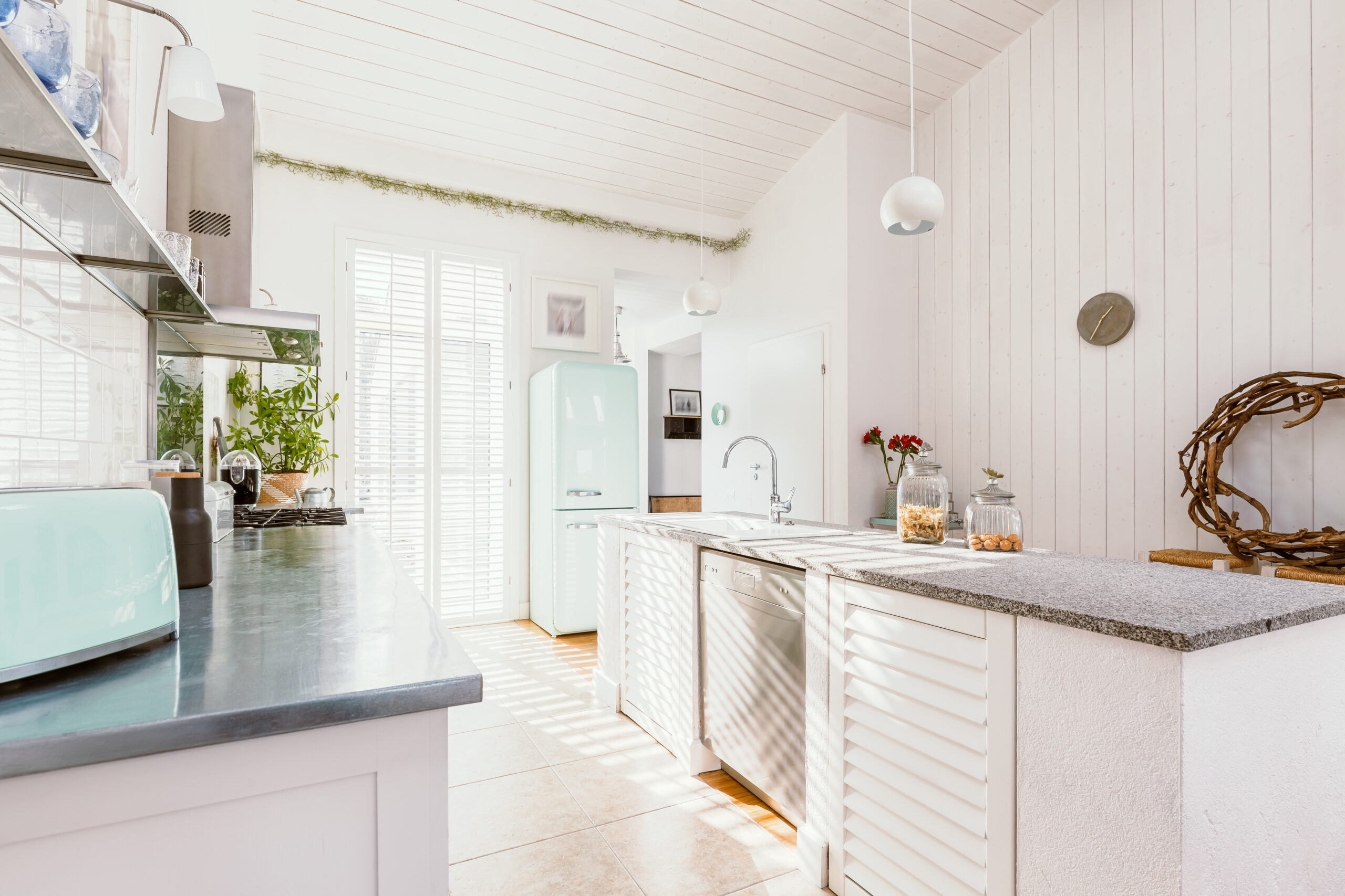 Bright wooden rustic kitchen with white furniture, big window, and fridge. Beach house kitchen remodels.