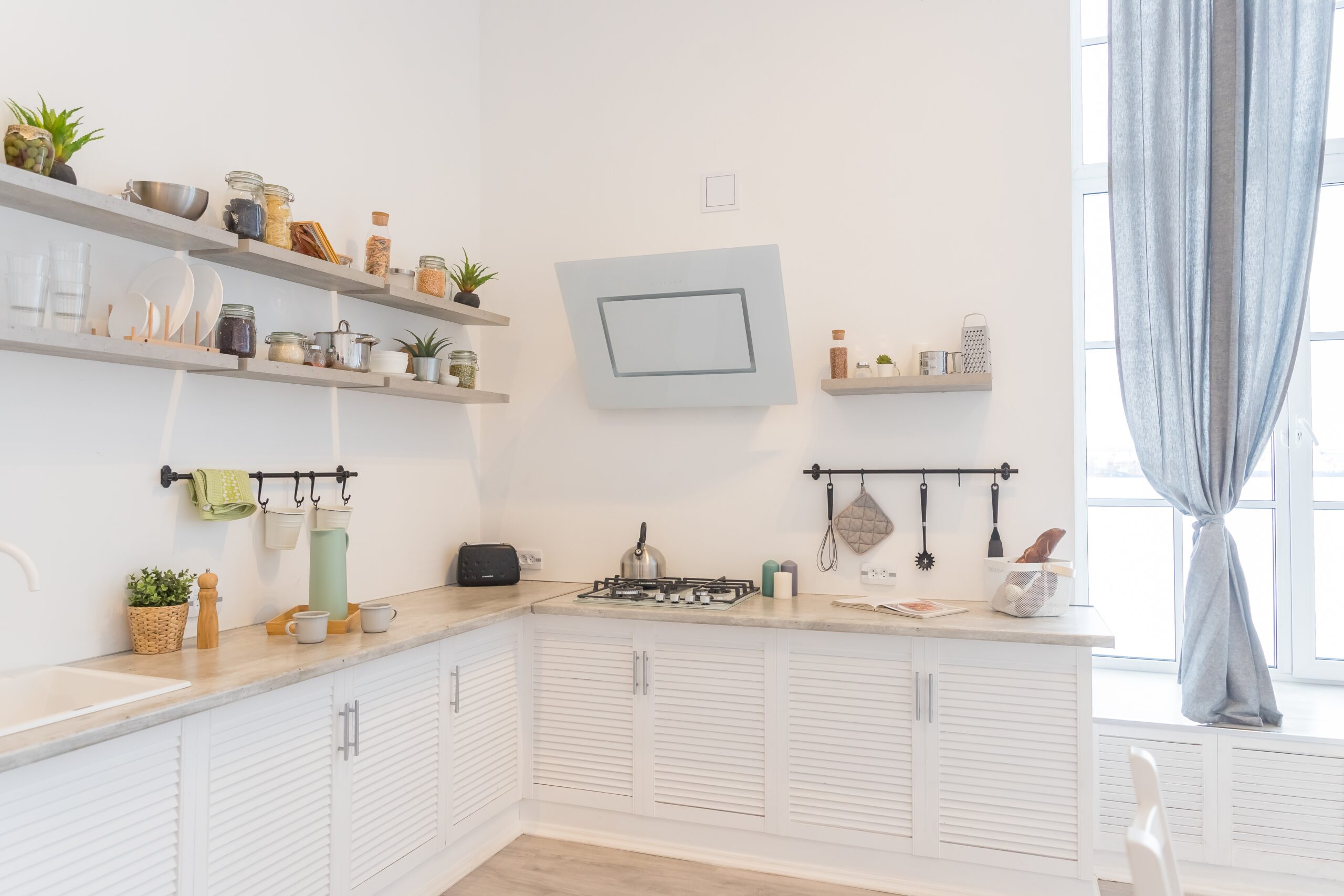 Corner of interior with white kitchen. Wooden shelves and window. Beach house kitchen remodel.